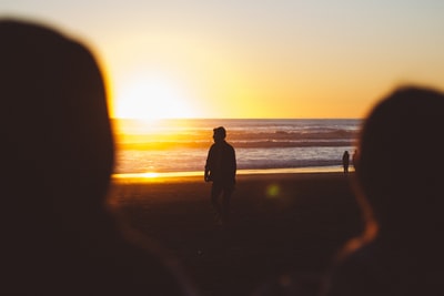 日落时分，一名男子站在海边的剪影照片